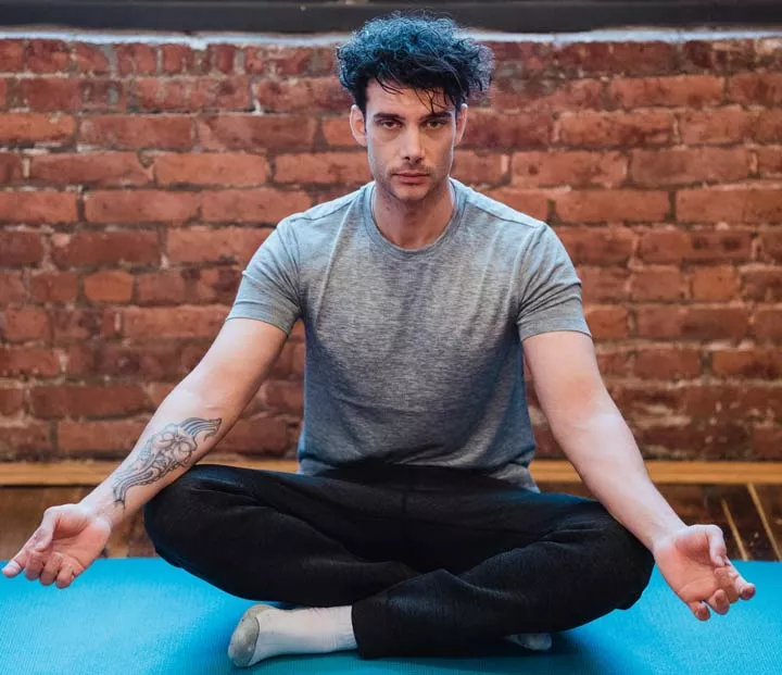 handsome dark-haired man sitting on blue mat in lotus position