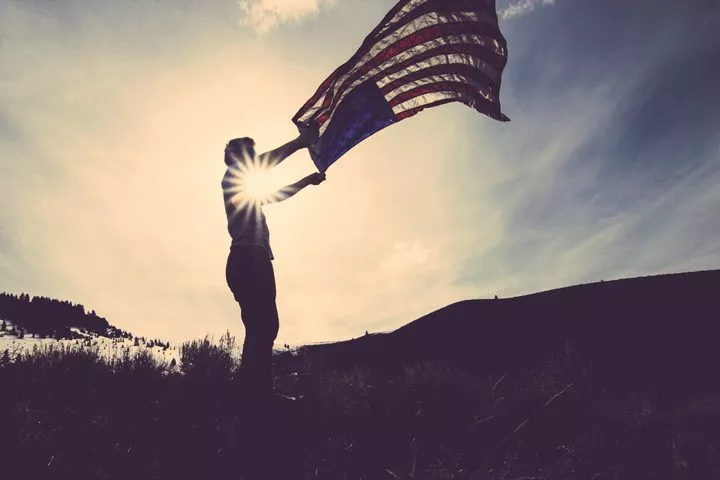 person waving a large American flag in the wind at sundown - veterans day