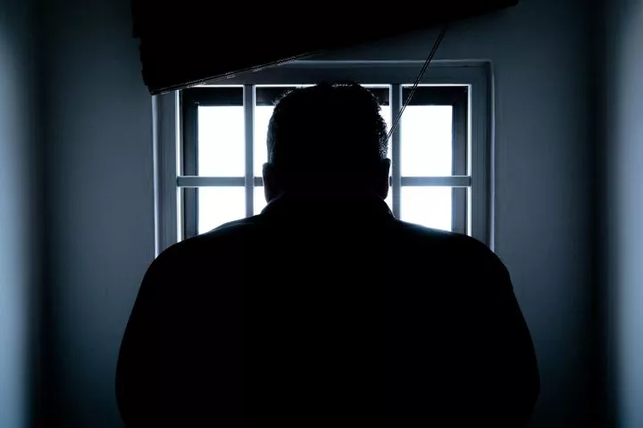 man standing in front of window in jail cell - incarceration
