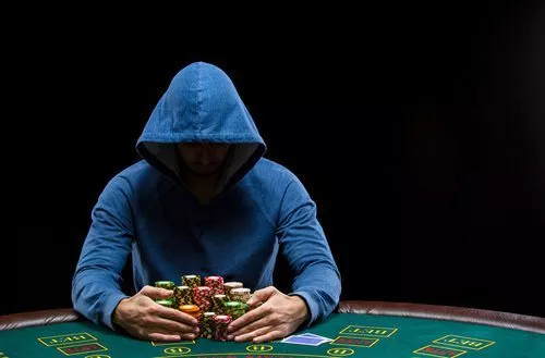 hooded man sitting at poker table with stacks of chips