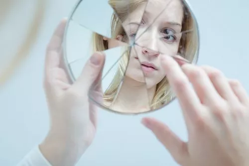 woman looking into broken mirror