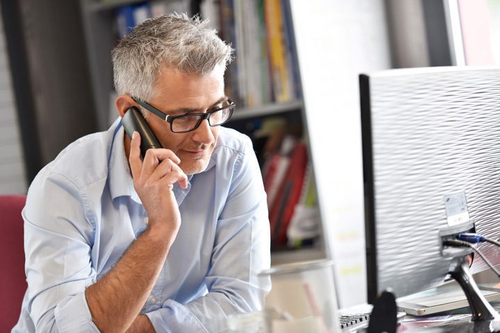 handsome senior man with glasses on the phone in his office - insurance