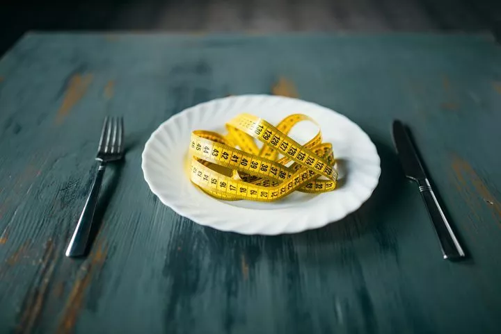 white plate with yellow tape measure on it, set on table with fork and knife - depression and eating disorders