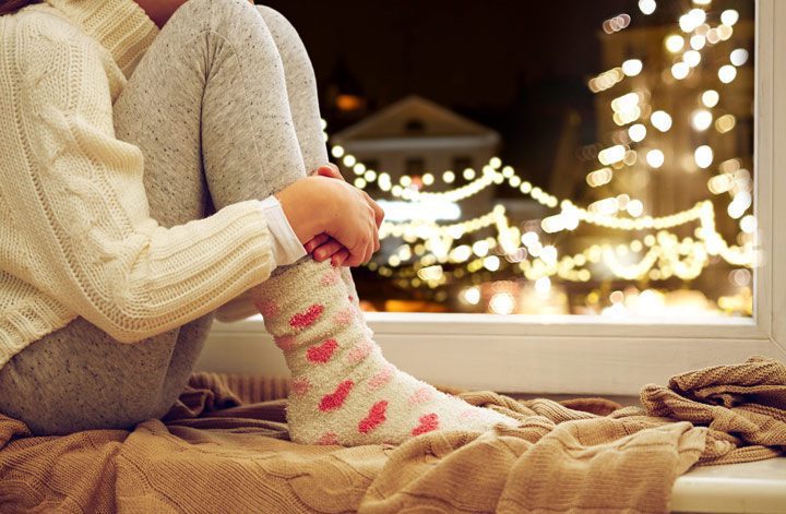 closeup of young woman with knees to chest in window nook - Christmas lights seen through window - loneliness