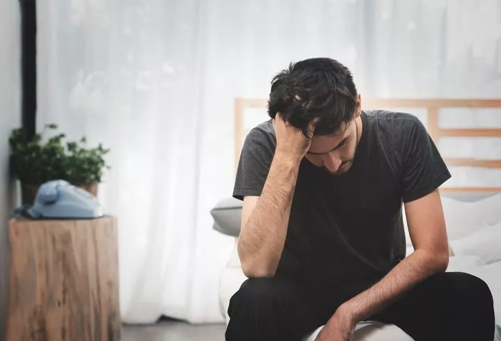 man sitting on the edge of his bed with hand in his hair looking stressed - anxiety and addiction