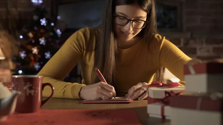 smiling woman writing notes or Christmas cards - holiday traditions