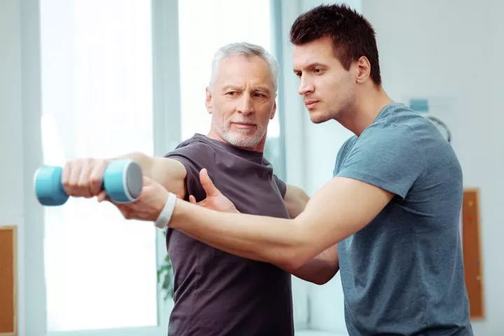 therapist helping man do exercises at physical therapy - pain management