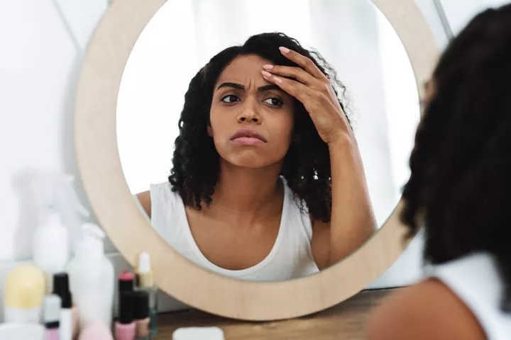 pretty African American woman looking in mirror at her face - body dysmorphia