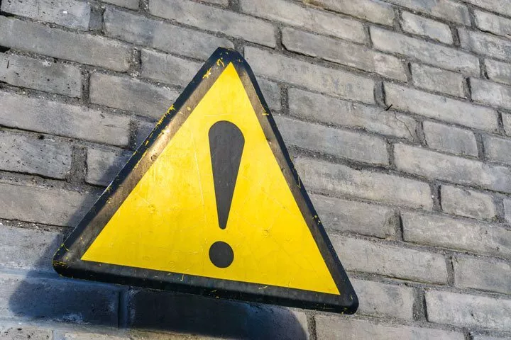 yellow and black triangular warning sign against brick wall - relapse symptoms