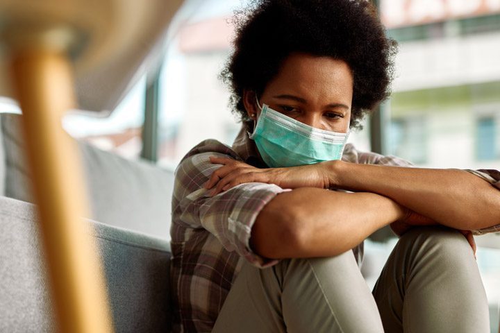 worried looking woman at home with mask on - COVID and mental illness