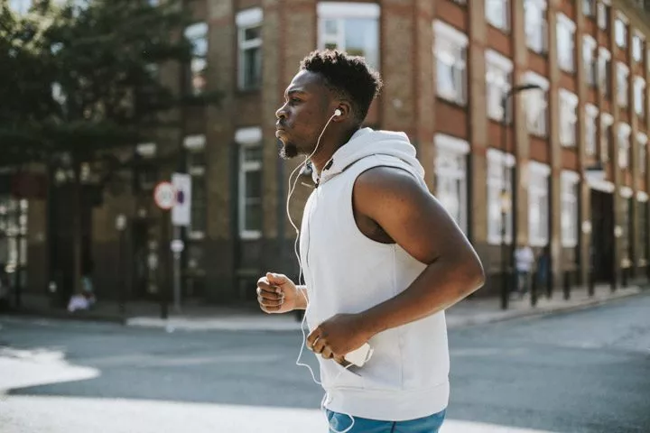 handsome middle age Black man jogging down city sidewalk - exercise addiction