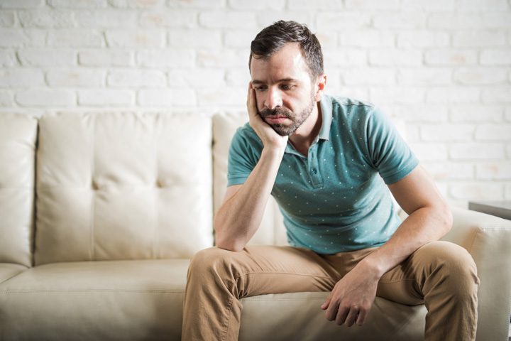 man in his forties sitting at home on his couch looking bored or sad - languishing