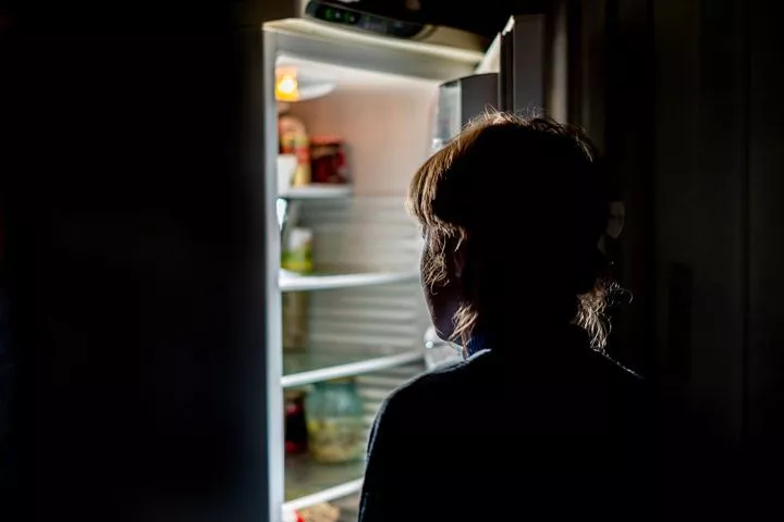 dark kitchen where woman is opening the fridge - Night-Eating Syndrome
